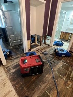 Red drying equipment in a flooded room, wood floors, exposed walls, blue dehumidifiers.