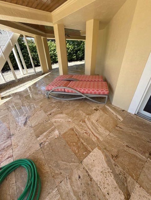 Outdoor patio with tile flooring, two chaise lounges, and green hose.