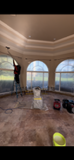 Person on ladder cleaning in a room with large arched windows and a detailed ceiling.