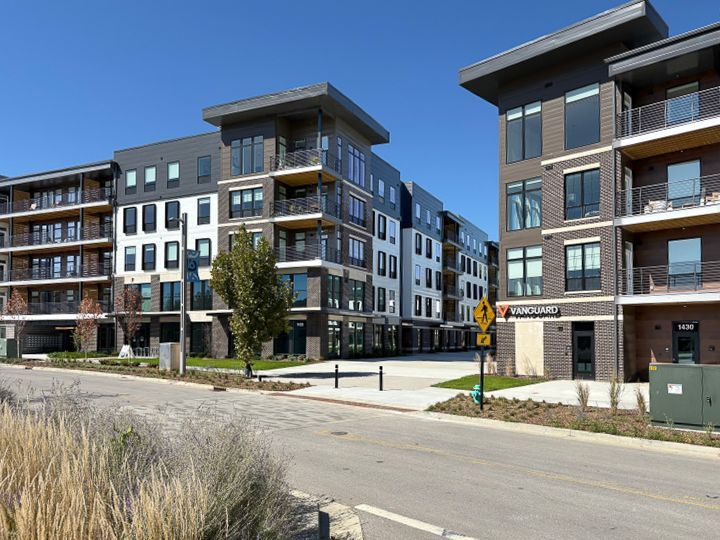Multi-story of Vanguard at 16 Tech with dark siding, balconies, and a sunny, clear sky.