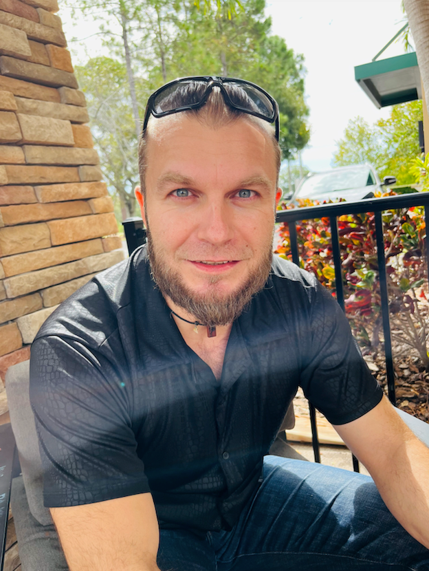 A man with a beard is wearing sunglasses and a black shirt.