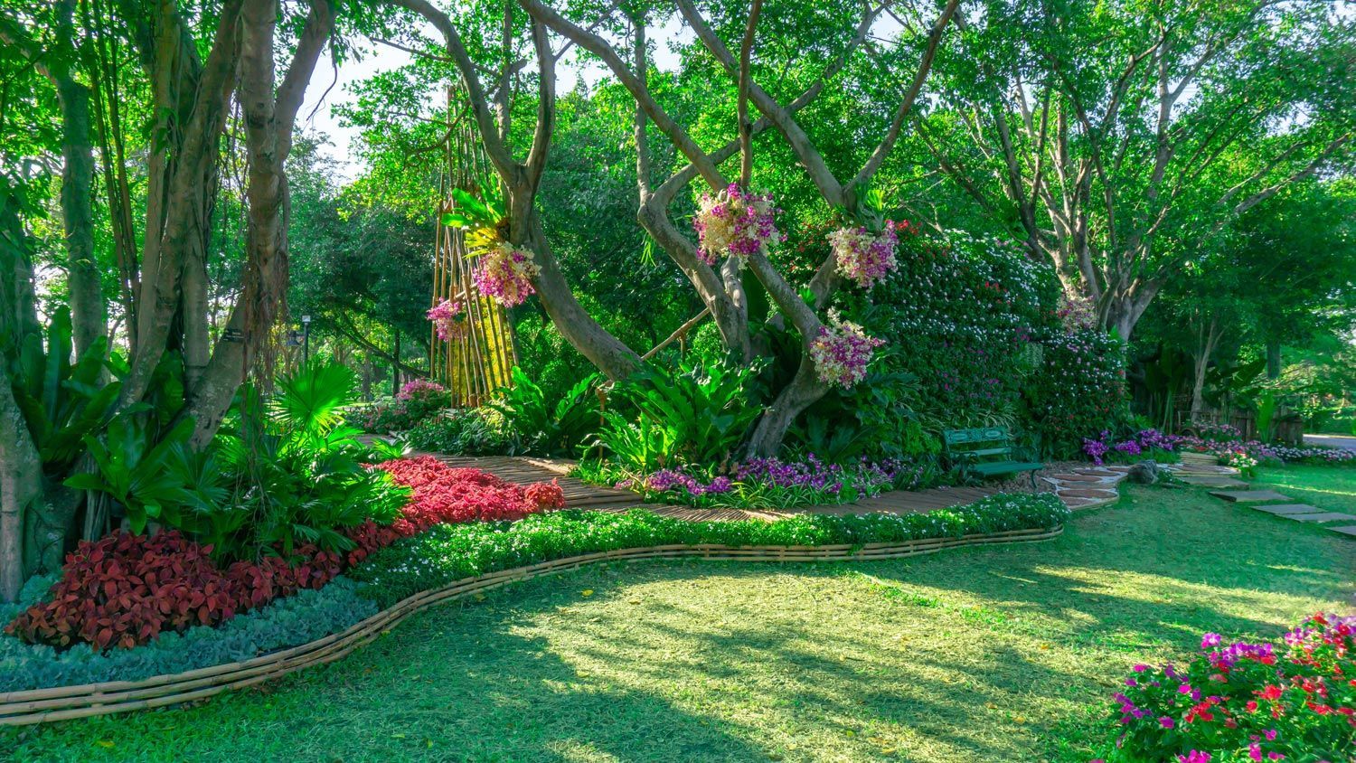 Lush garden with green trees, pink flowers, and a sunlit lawn