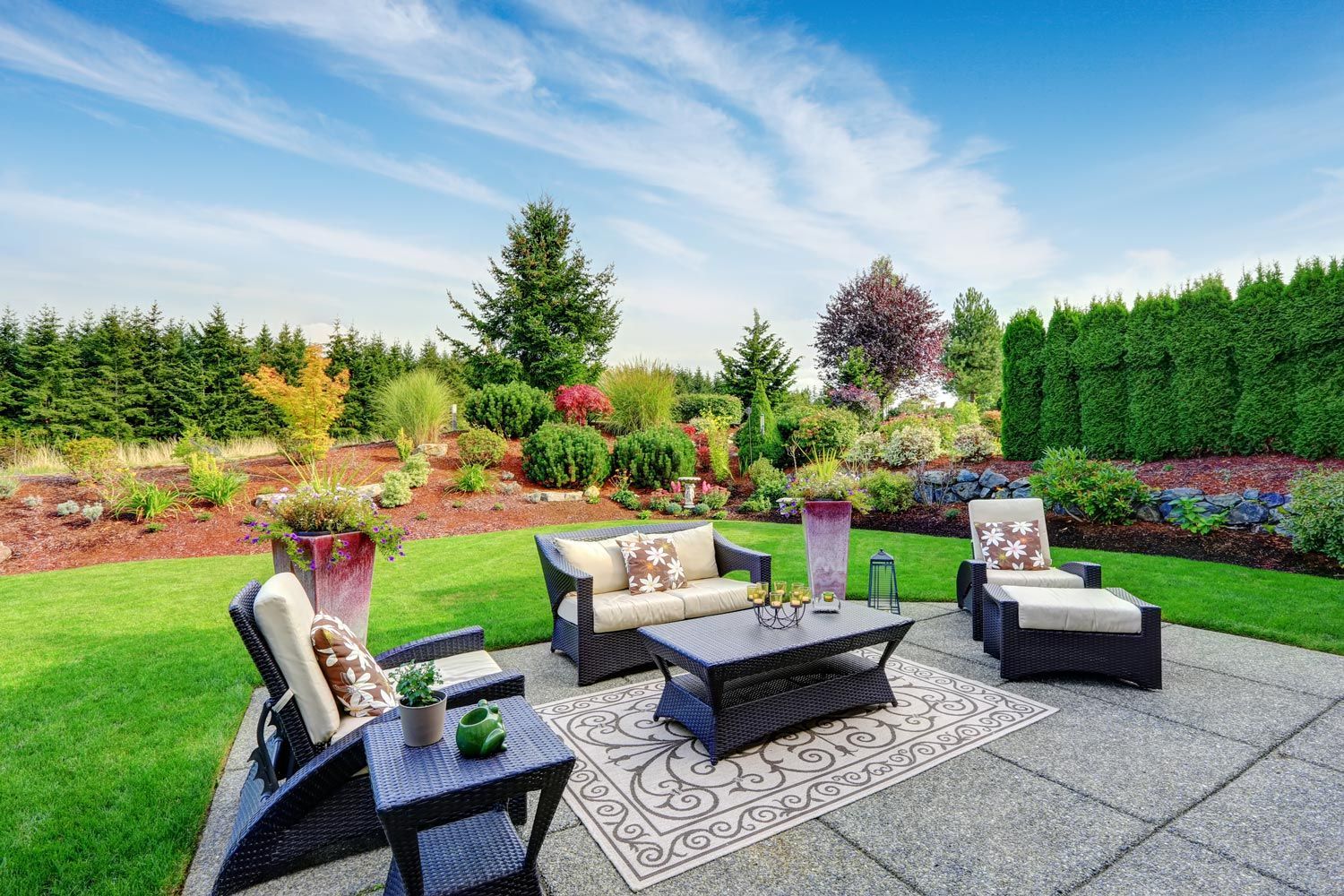Patio seating area in a landscaped backyard with modern chairs, coffee table, and colorful flower beds