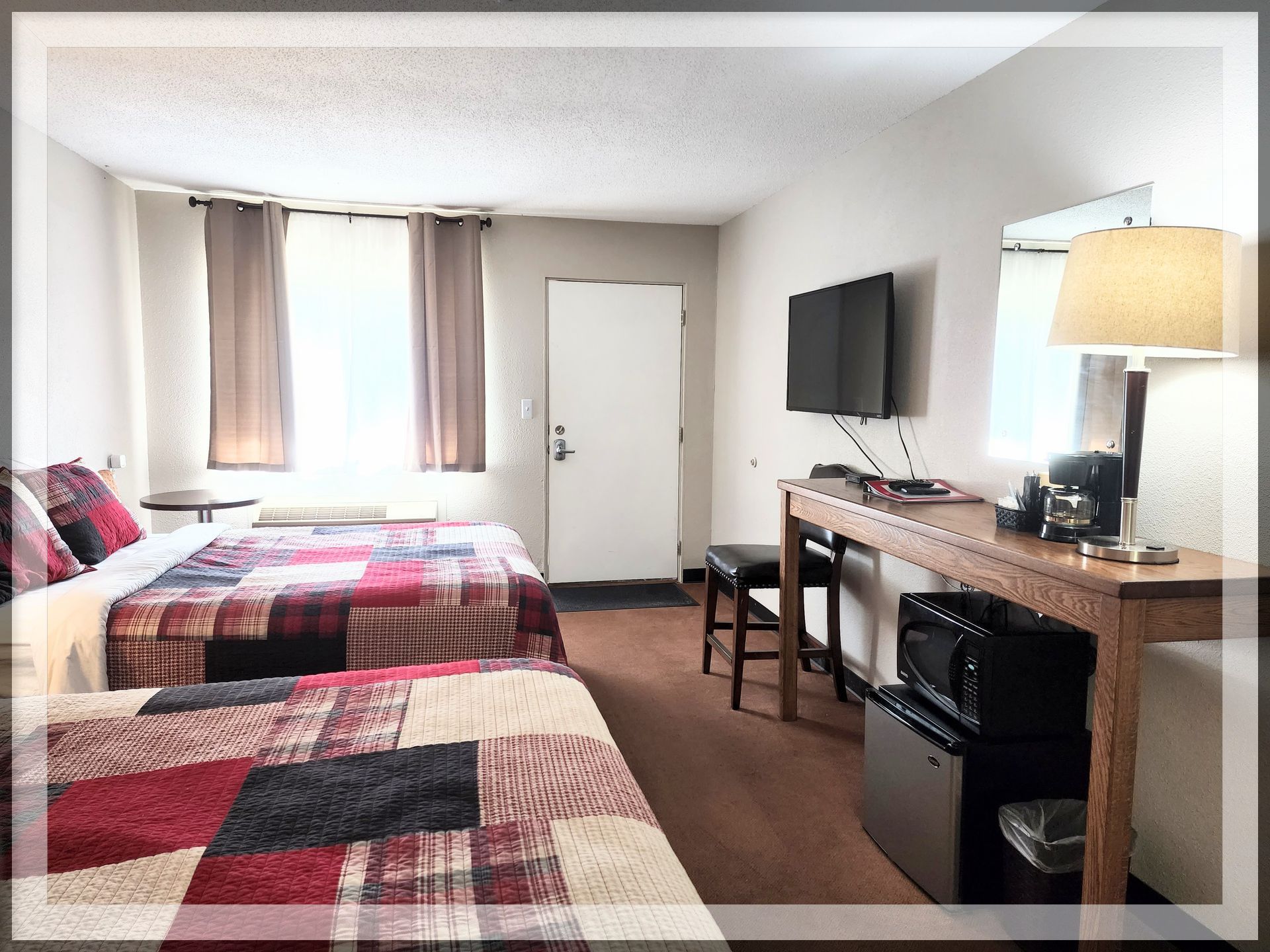 This is an image of a bedroom, wall-mounted TV, and front door in a remodeled Double Queen Room.