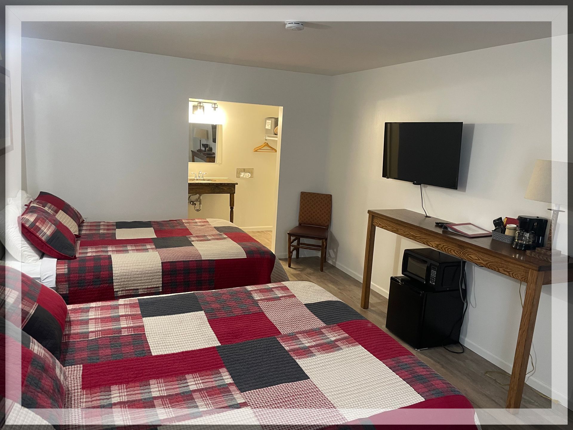 This is an image of the bedroom with the main bathroom entrance and wall TV in a remodeled Double Queen Room.
