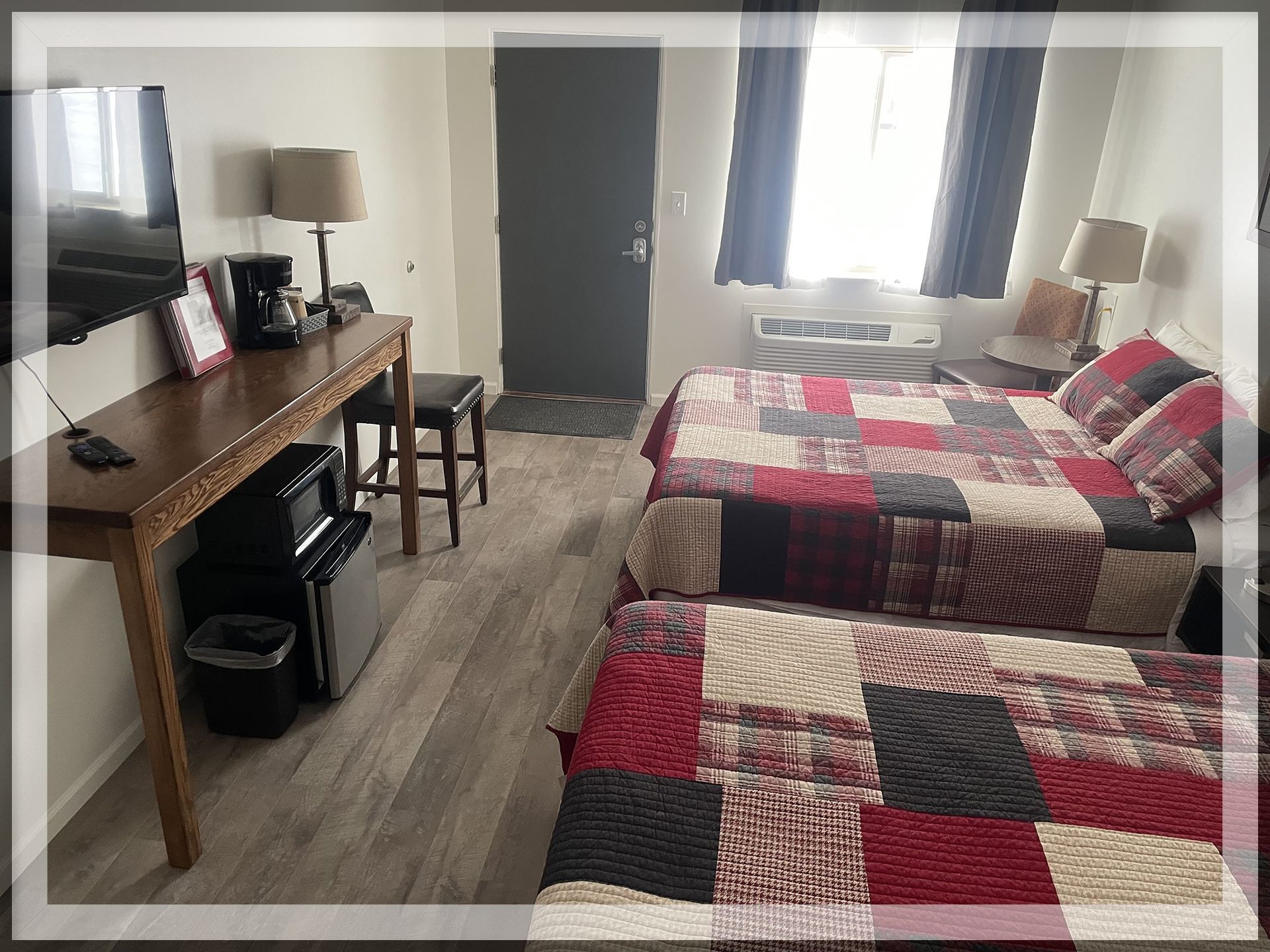 This is an image of the bedroom with the main window and table of a remodeled Double Queen Room.