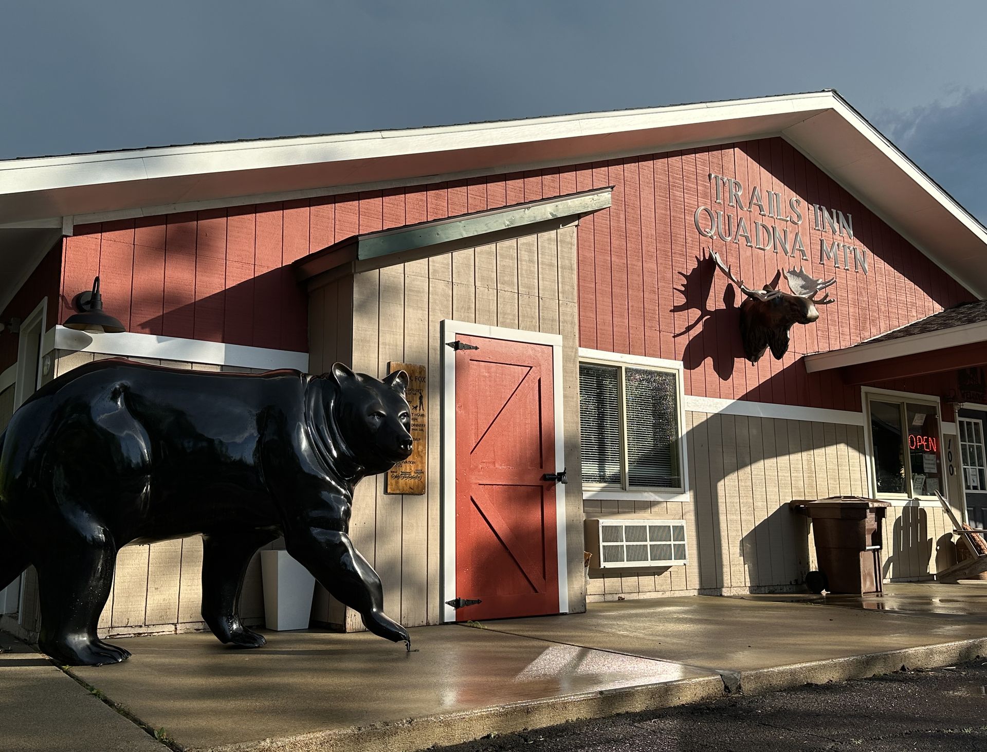 A corner image of The Trails Inn Quadna Mountain Motel office. An image of the front office of The Trails Inn Quadna Mountain Motel with a bear statue.