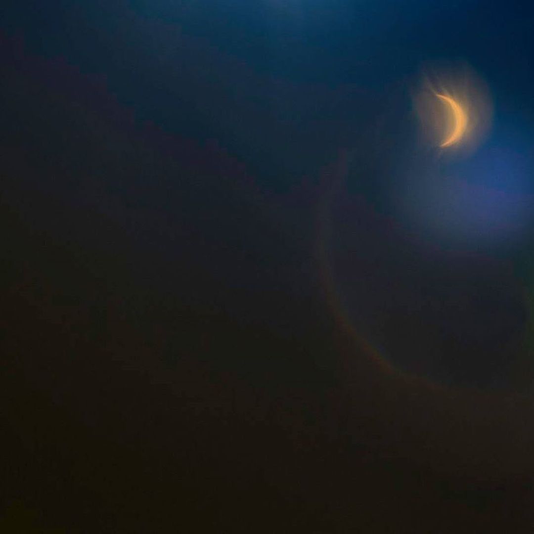 Night sky with a crescent moon and lens flare. Deep blue and orange light.
