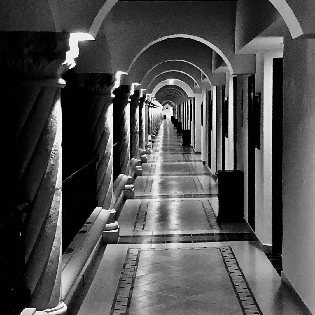 Hallway with arched ceilings, columns, and receding perspective, leading to a bright light at the end.