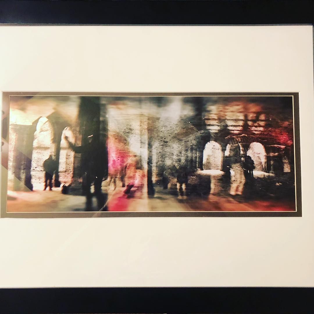 Blurred cityscape artwork, framed. Silhouettes of people amid arches and colorful lights.