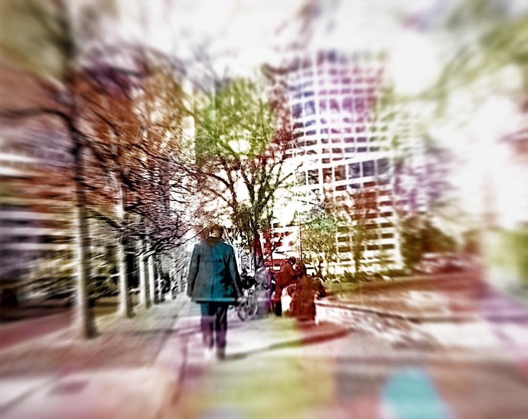 Person walking on a sidewalk near trees and buildings; blurred, colorful effect.