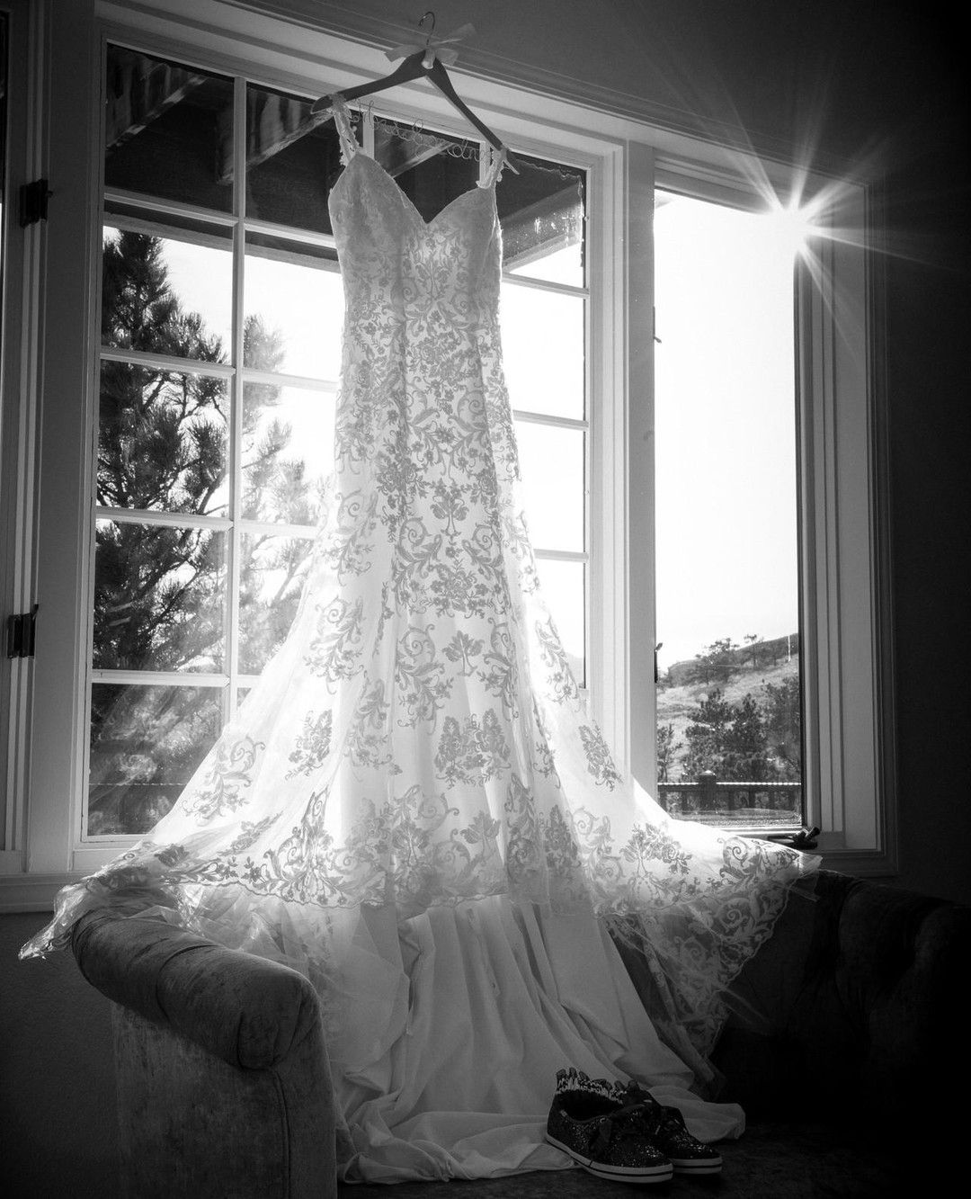 Wedding dress hanging in window, sunlight streaming through, black and white.