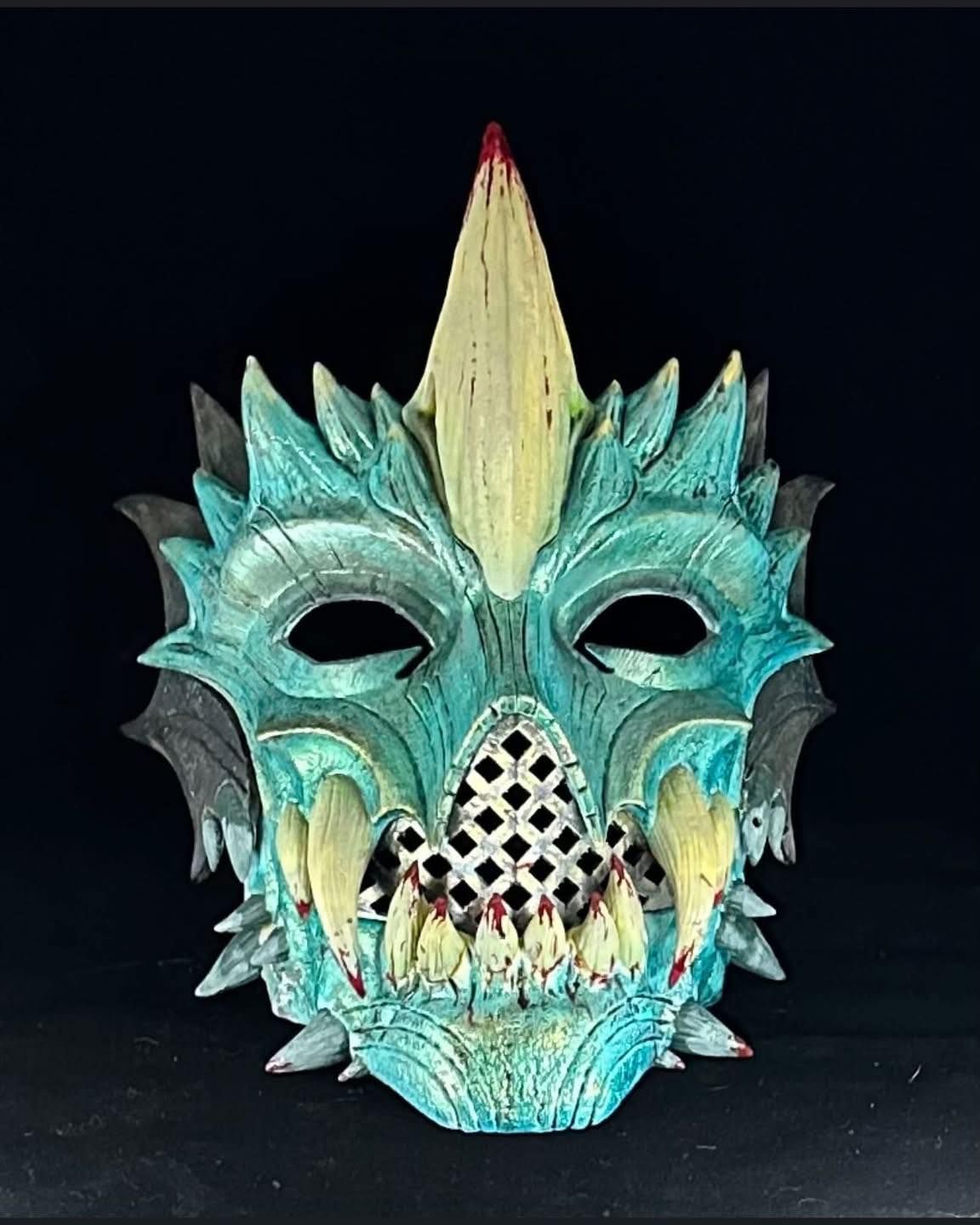 Blue and yellow aquatic-themed mask with sharp teeth, a central spike, and a lattice mouth over a black background.