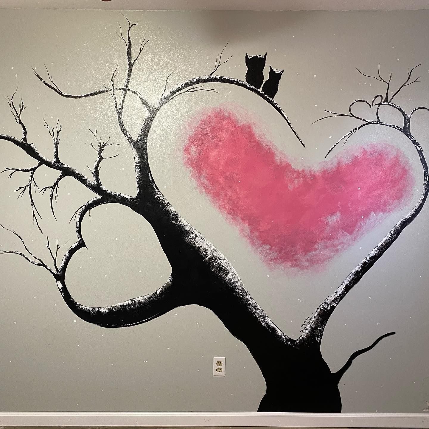 Black tree mural with pink heart, two owls on gray wall.