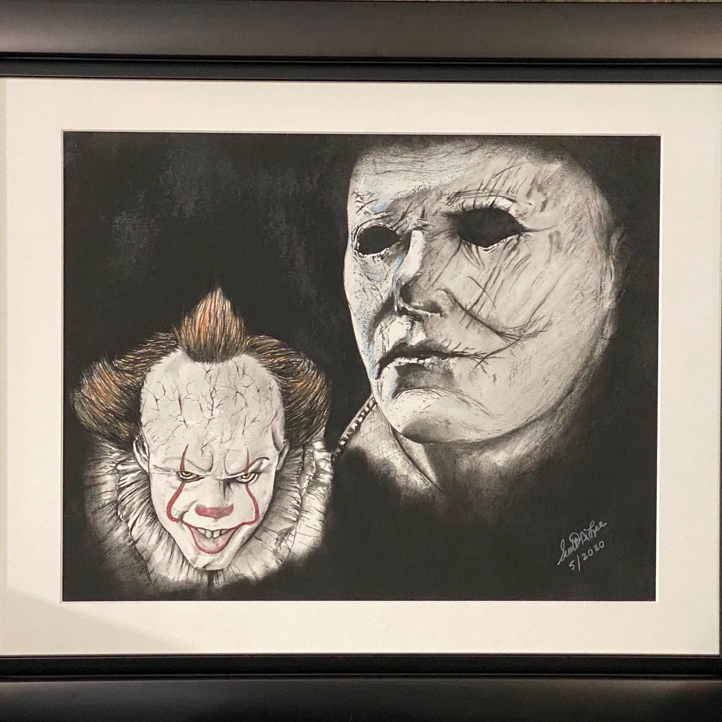 Charcoal drawing of Pennywise the clown and Michael Myers on black background, framed.