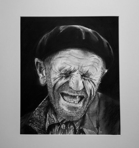 Charcoal portrait of a man, eyes squeezed shut, mouth open in a laugh, wearing a beret.