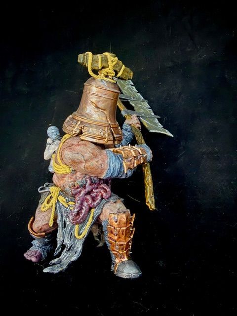 Figurine of a monstrous warrior with a bell-shaped helmet, wielding a large axe. Beige, blue, and brown tones.