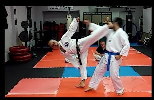Woman in white gi applying armbar on man in gray pants, on white background.