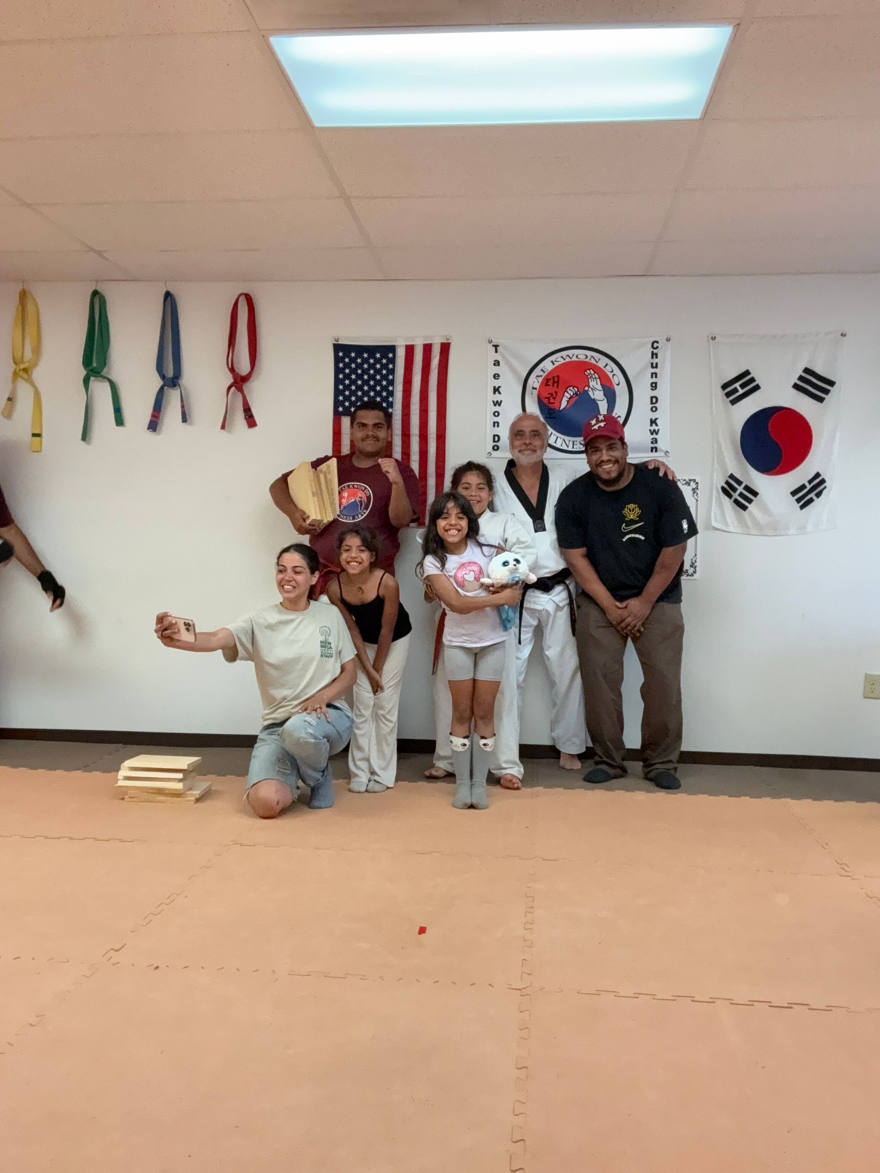 Children in white martial arts uniforms practicing kicking with pads in a gym.