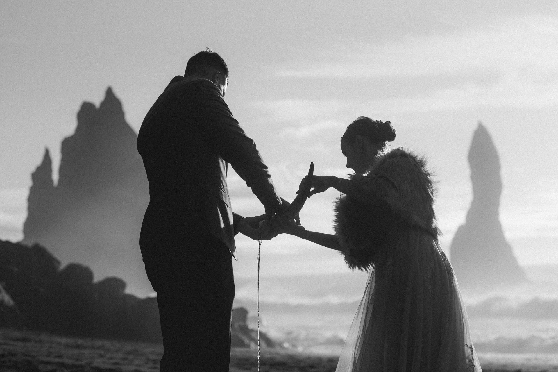 A black and white photo of a bride and groom making a heart shape with their hands.