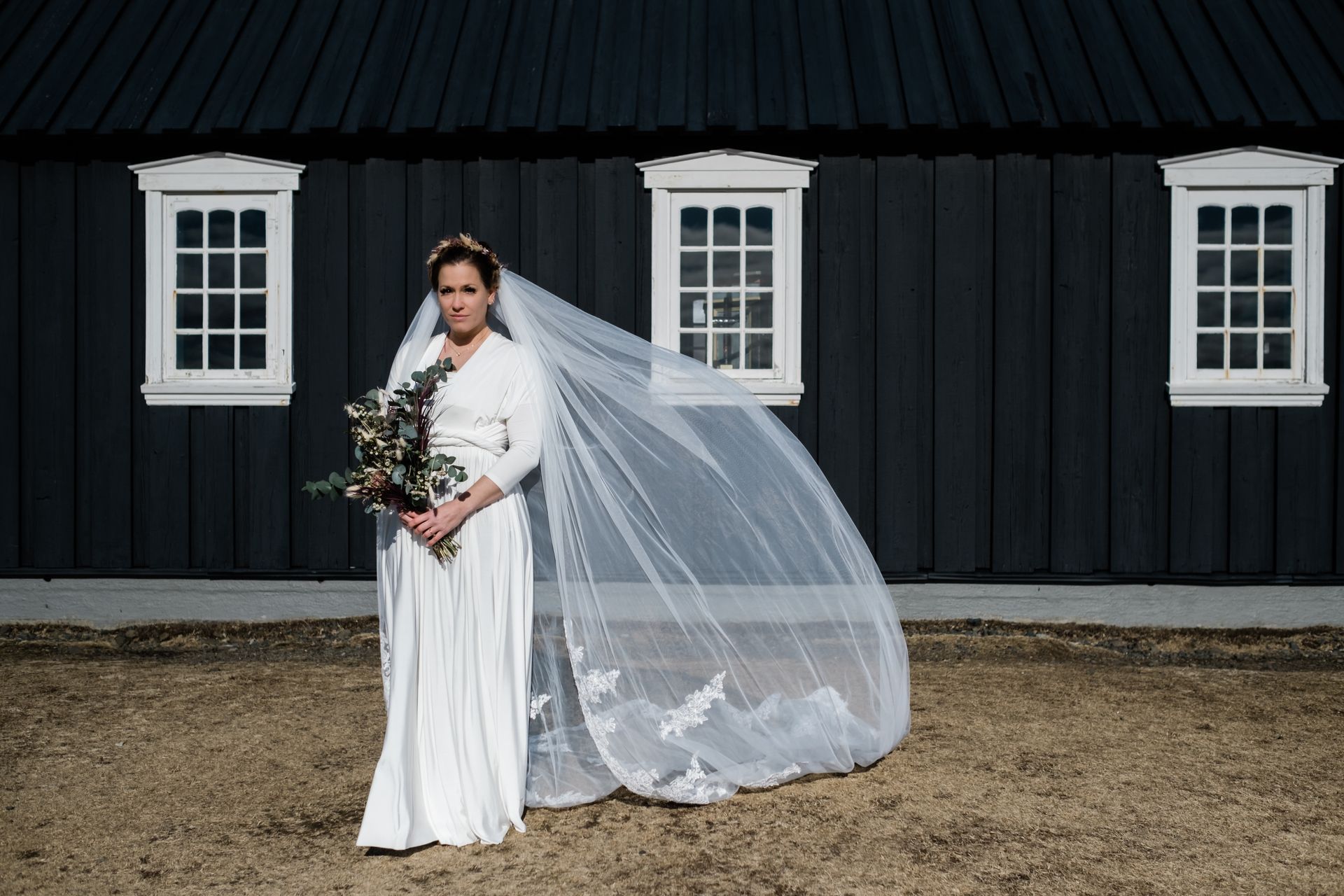 A bride in a white dress and veil is standing in front of a black building.