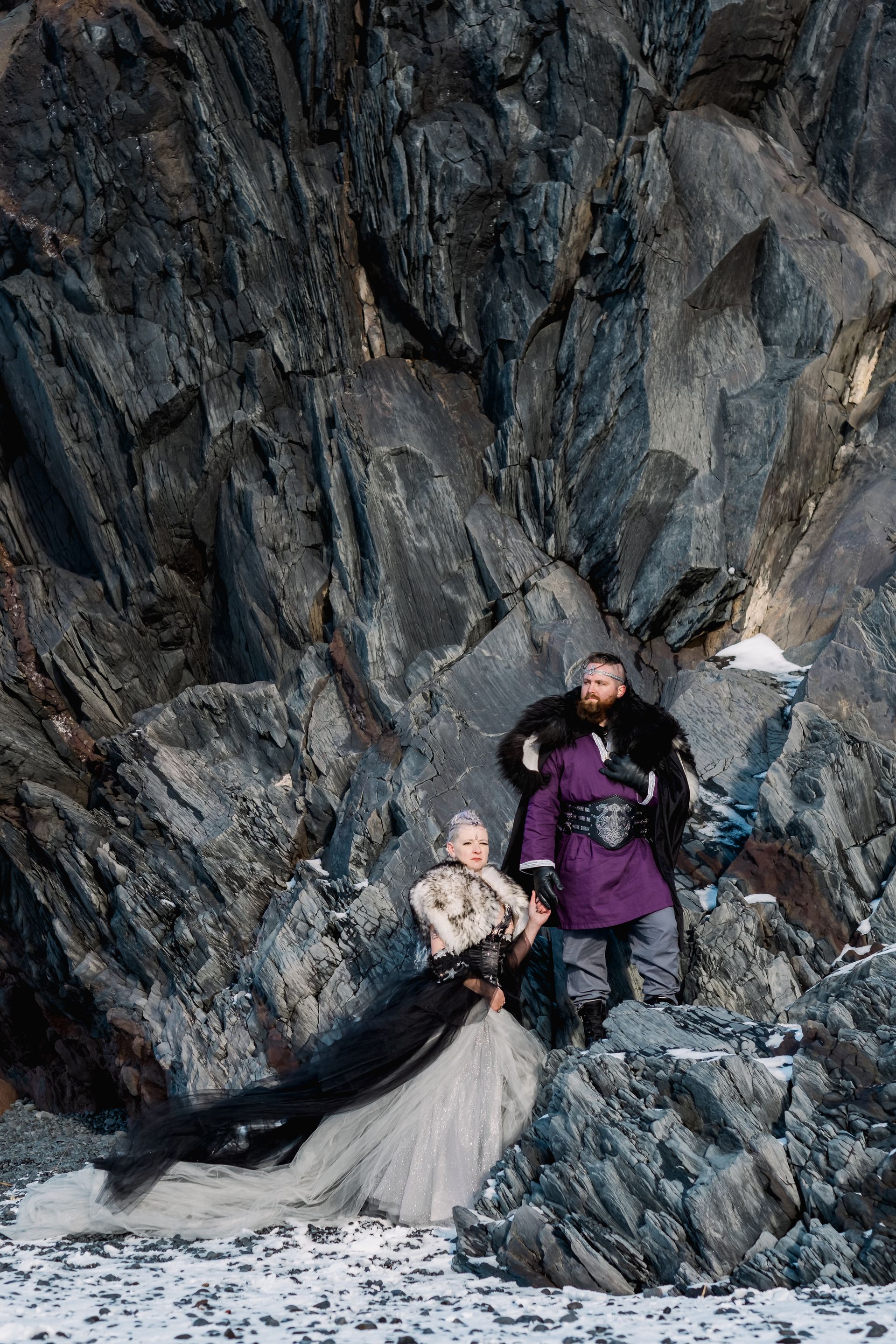 A man and a woman are standing on top of a rocky cliff.