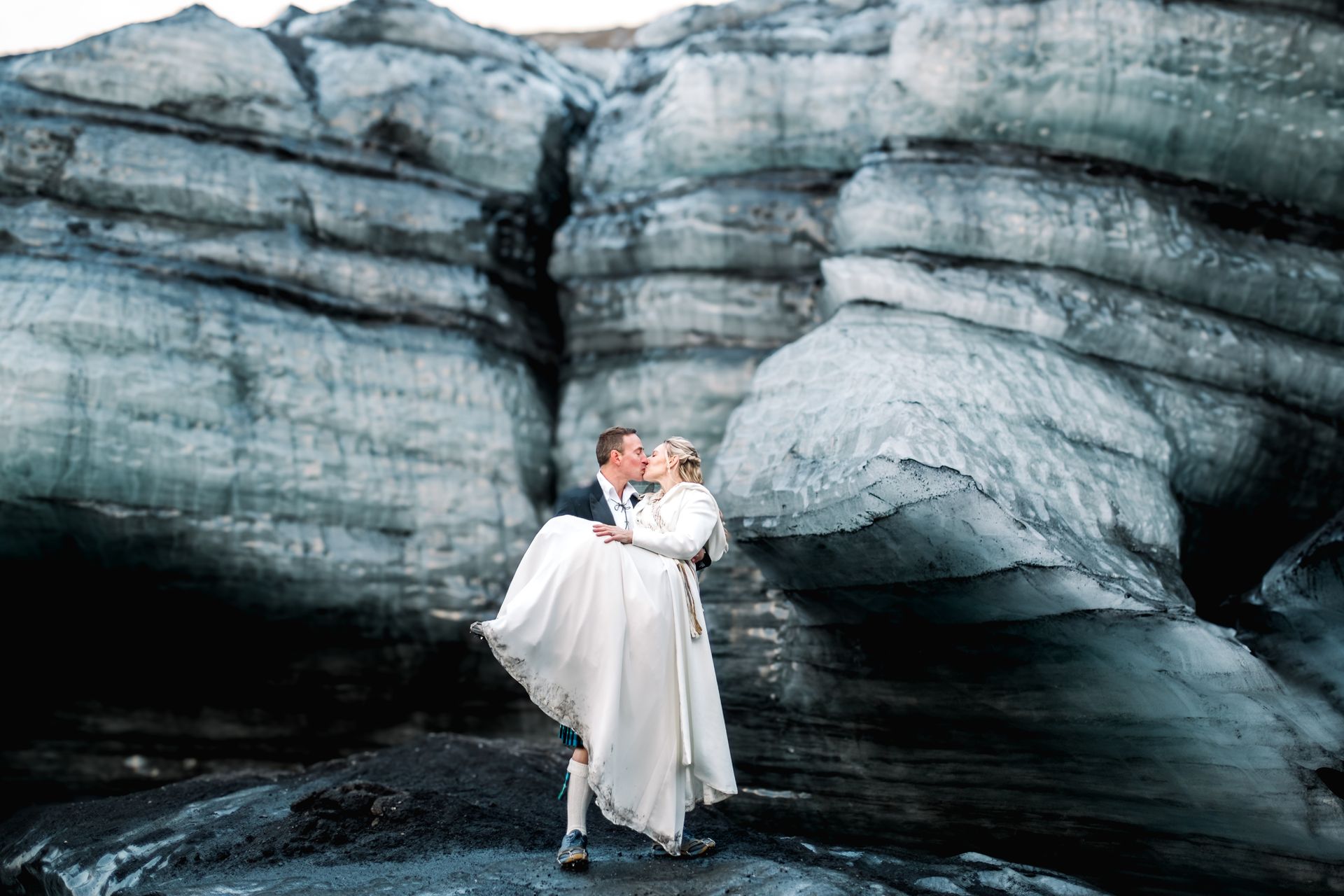 A bride and groom are kissing in front of a large rock formation.