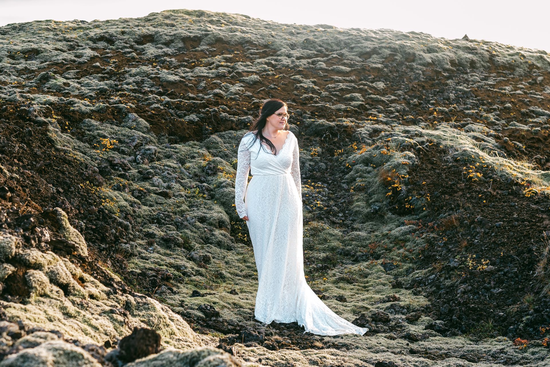 A woman in a white dress is standing on top of a rocky hill.