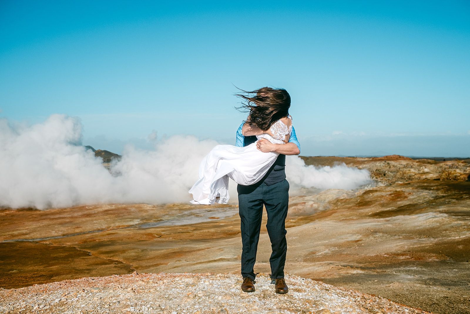 A couple elopes at a red-roofed A-frame cabin in snowy Iceland, surrounded by stunning blue skies and rugged scenery.