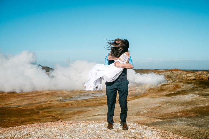 A couple elopes at a red-roofed A-frame cabin in snowy Iceland, surrounded by stunning blue skies and rugged scenery.