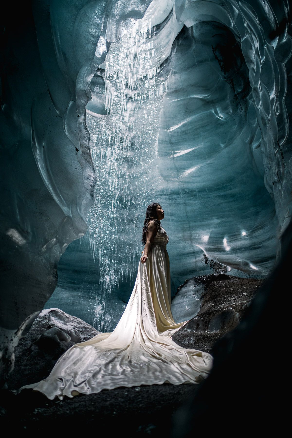 A woman in a long white dress is standing in an ice cave.