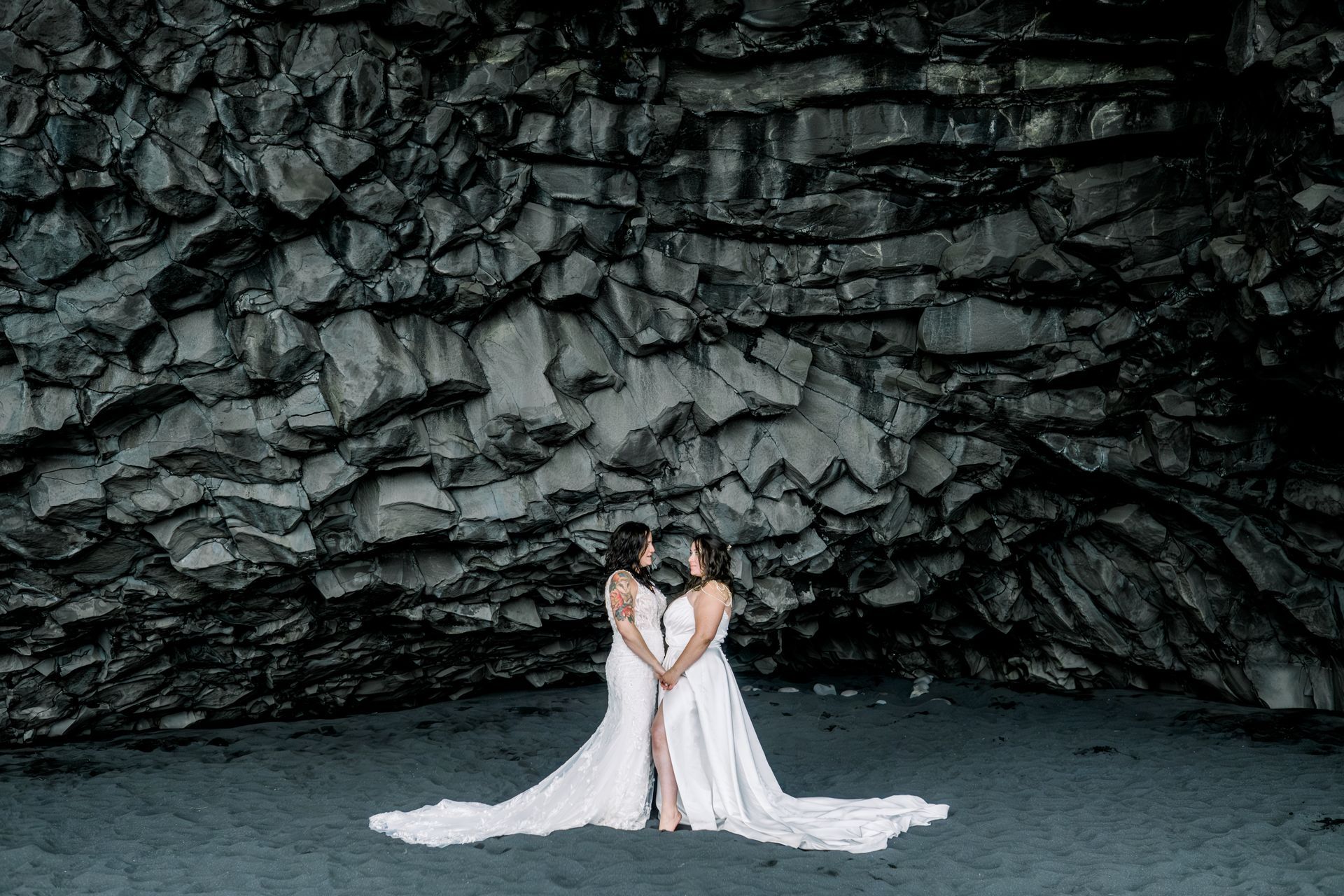 Two women in wedding dresses are standing next to each other on a beach.