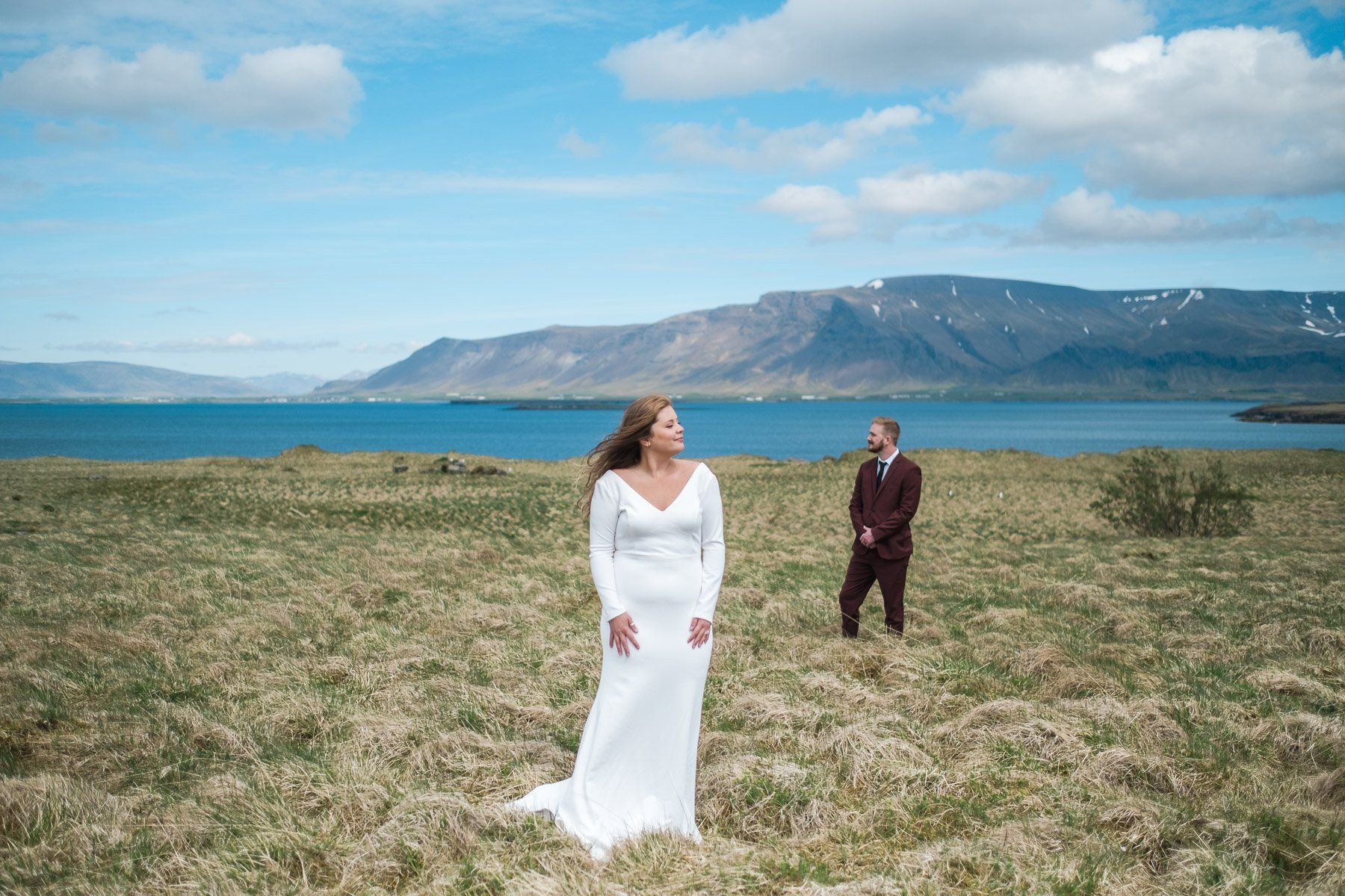 A bride and groom are standing in a field with mountains in the background in Iceland.