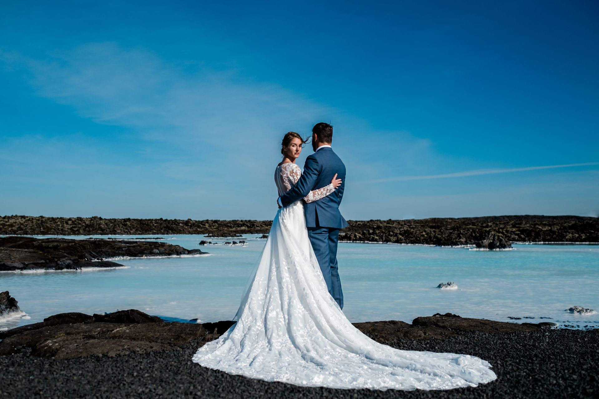 A bride and groom are posing for a picture in front of a lake.
