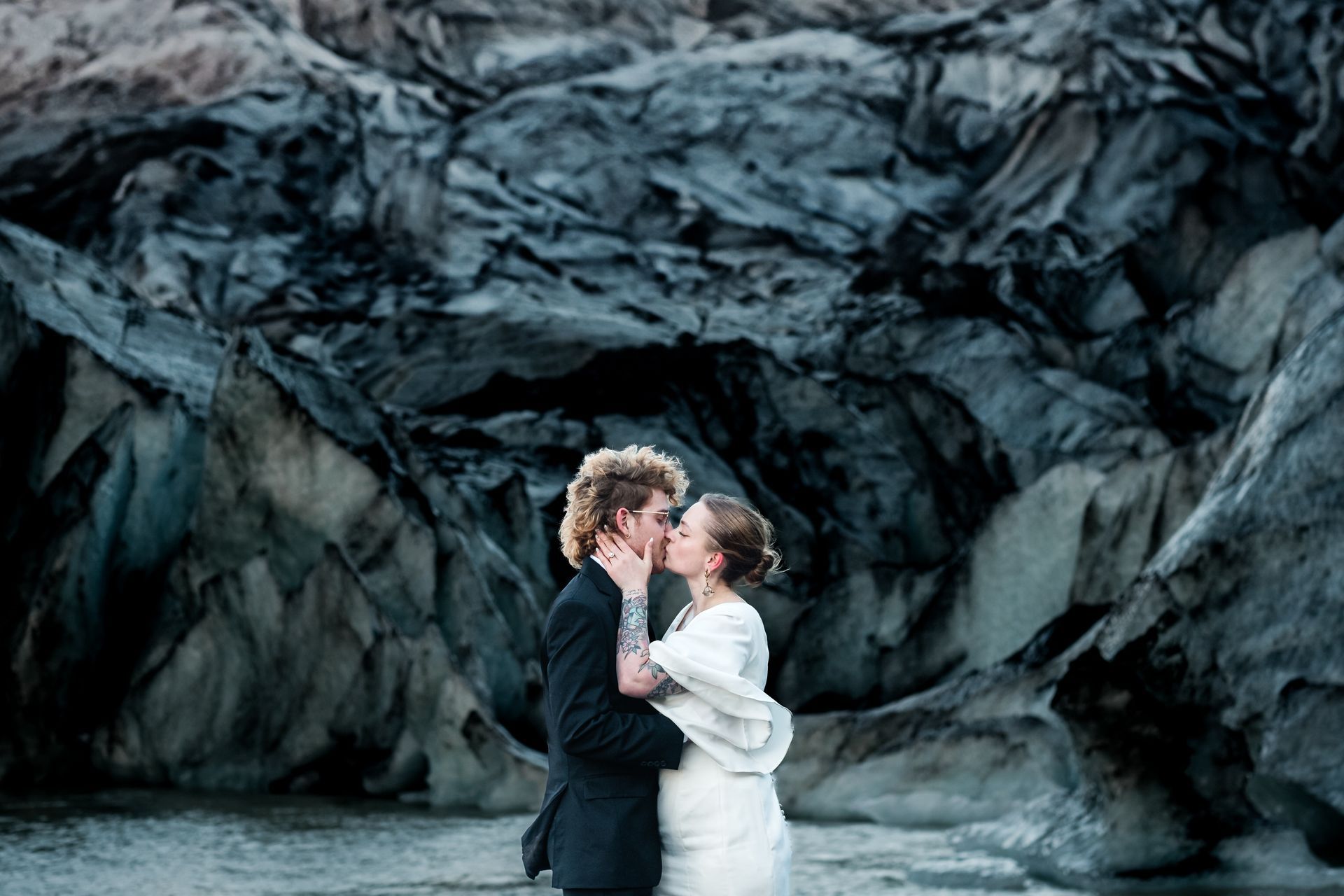 A bride and groom are kissing in front of a large rock formation.
