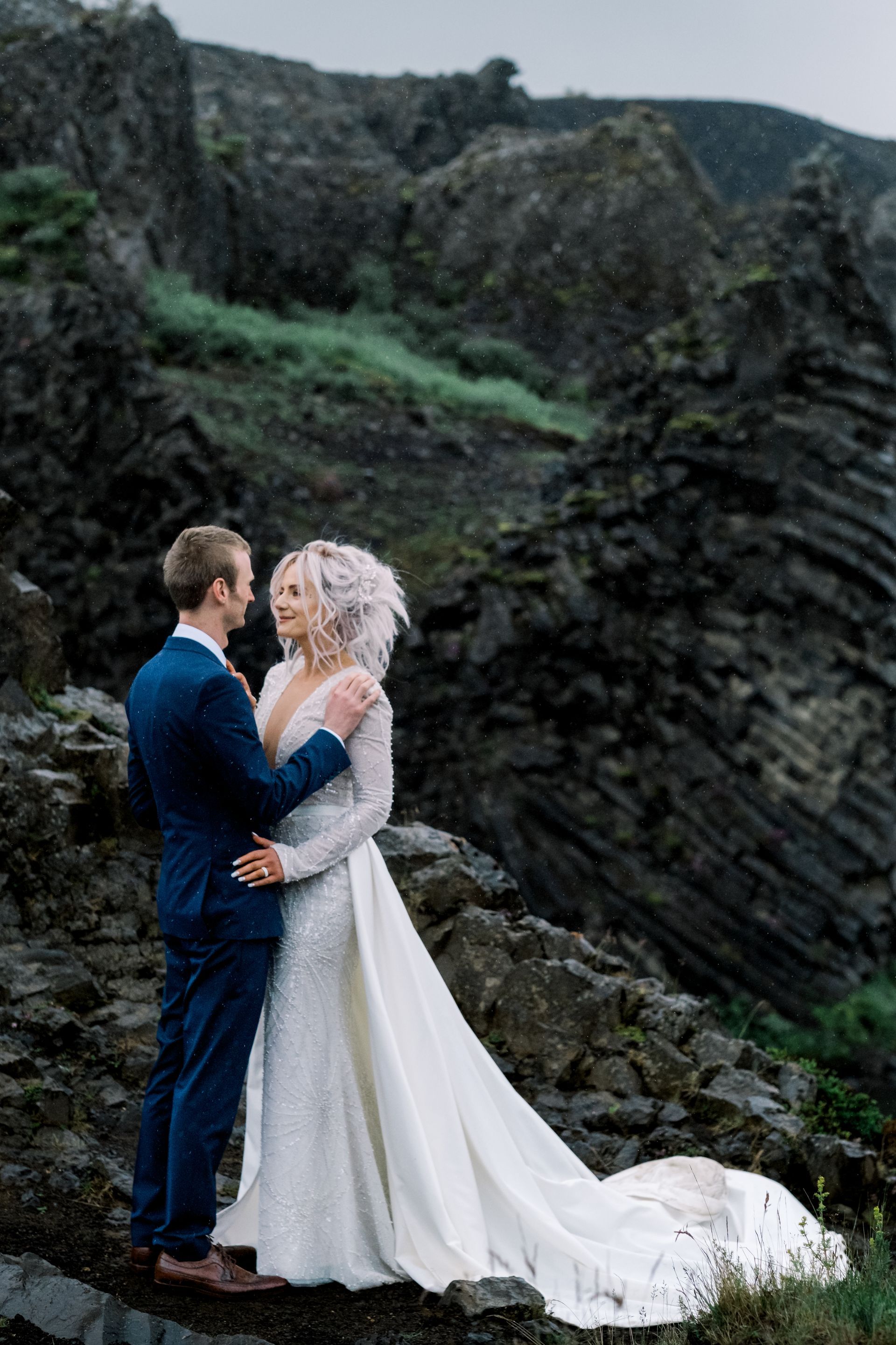 A bride and groom are standing on top of a rocky hill.