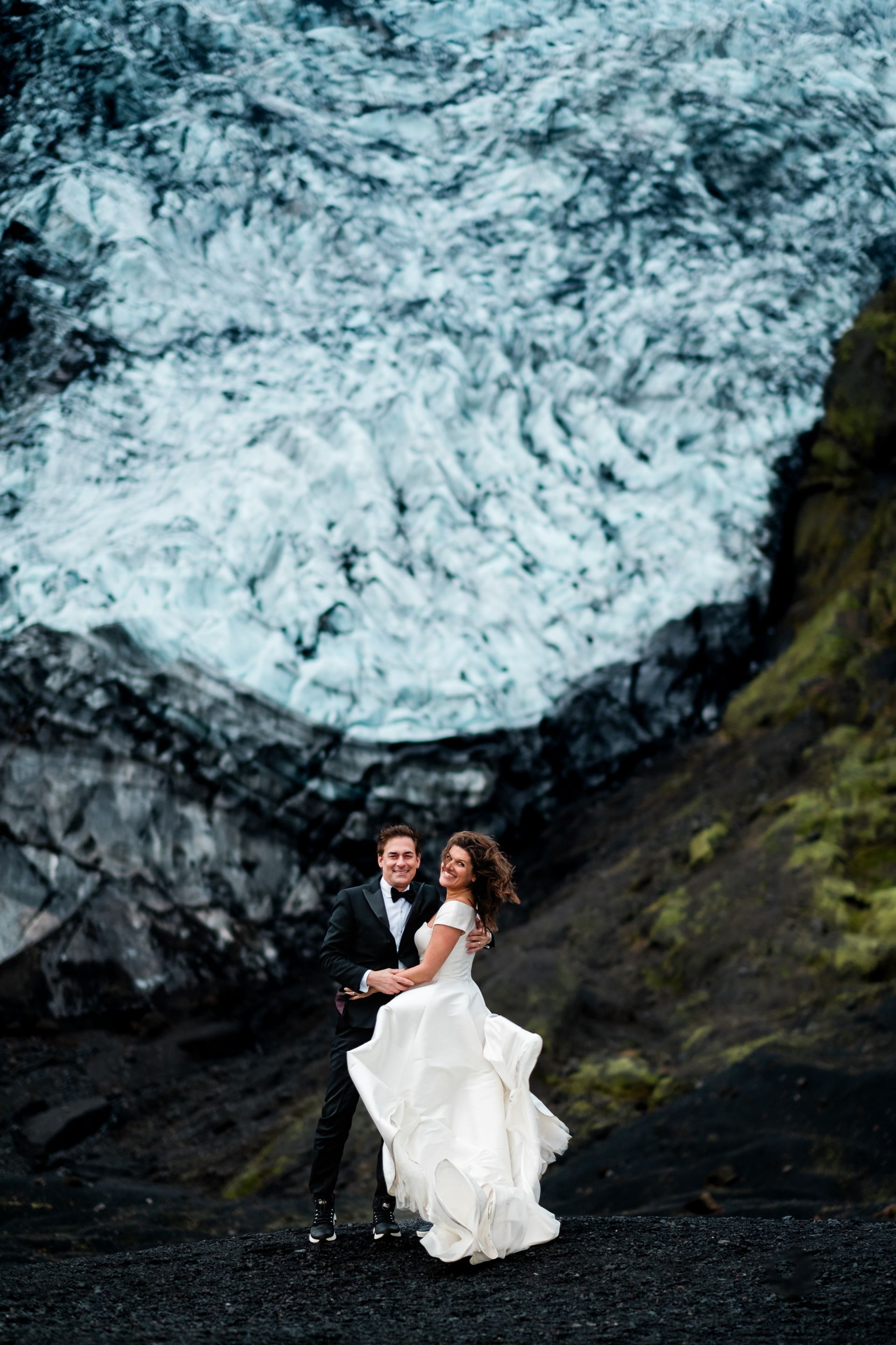 A bride and groom are posing for a picture in front of a waterfall.