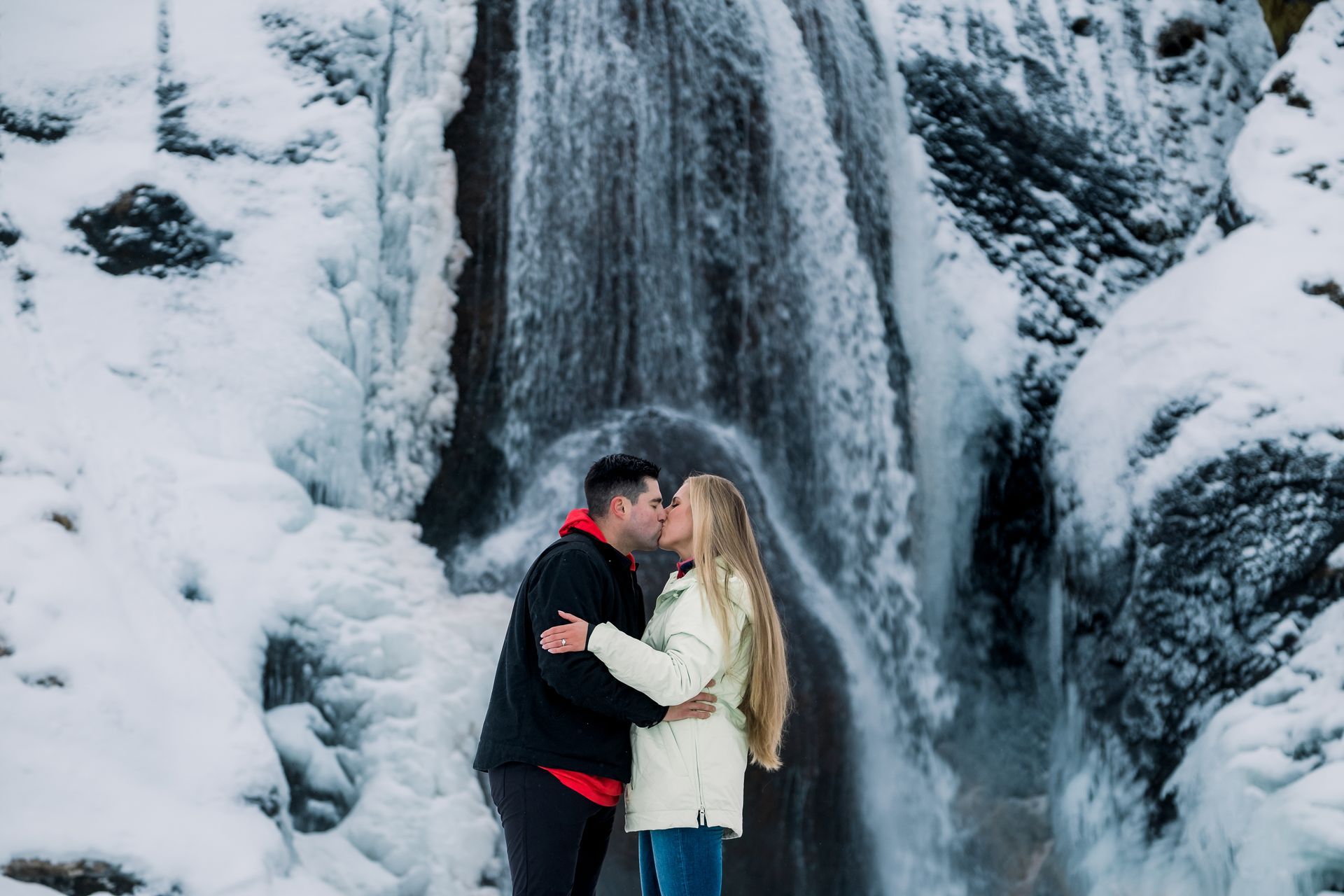 A man and a woman are kissing in front of a waterfall.