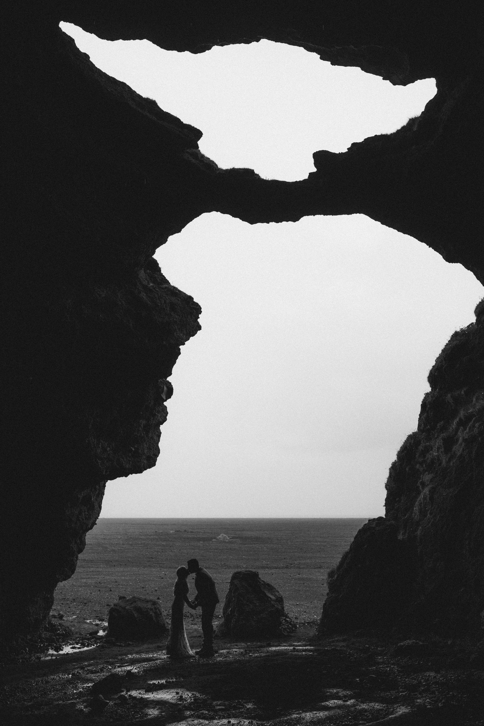 A black and white photo of a couple kissing in a cave