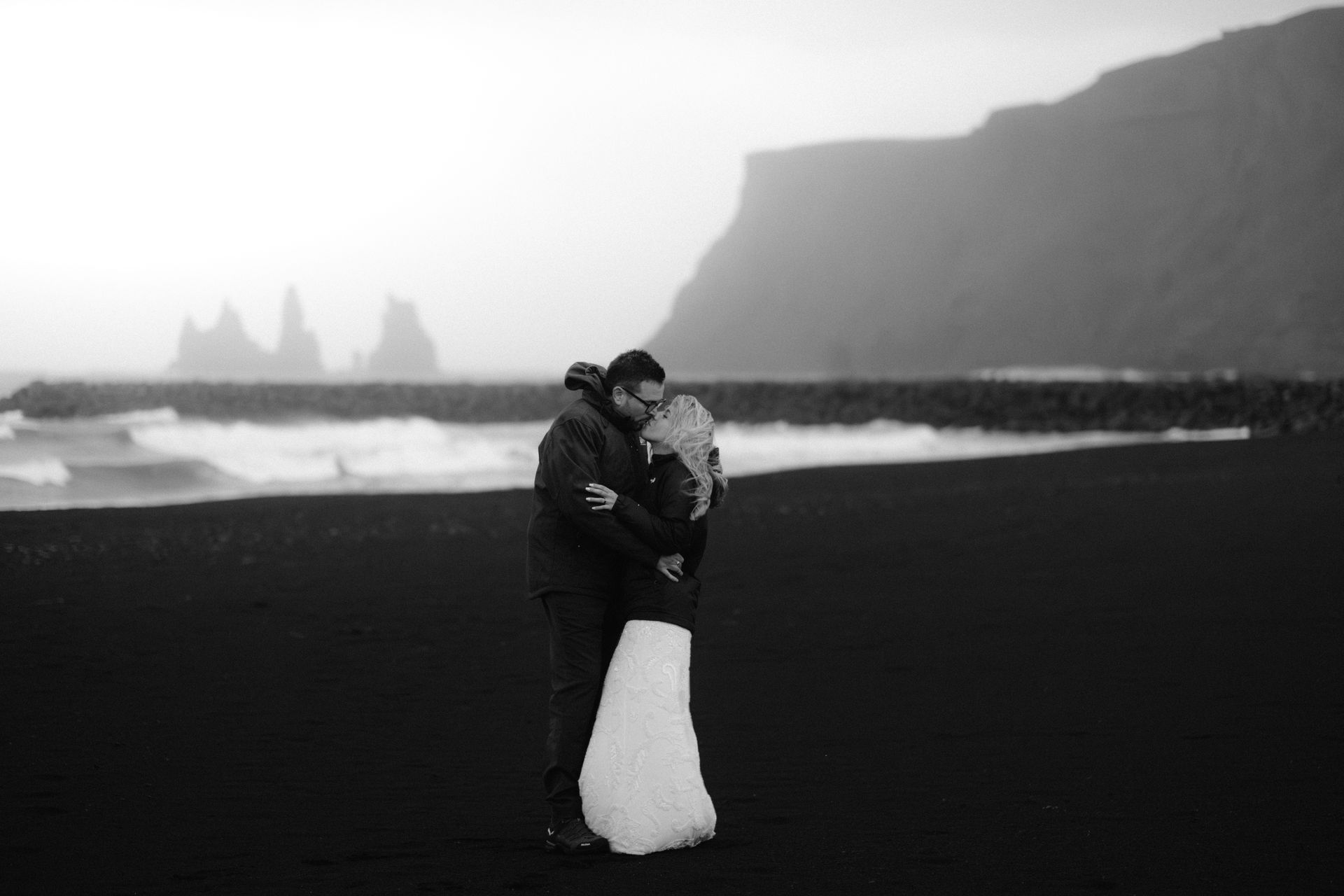 A black and white photo of a bride and groom hugging on a beach.