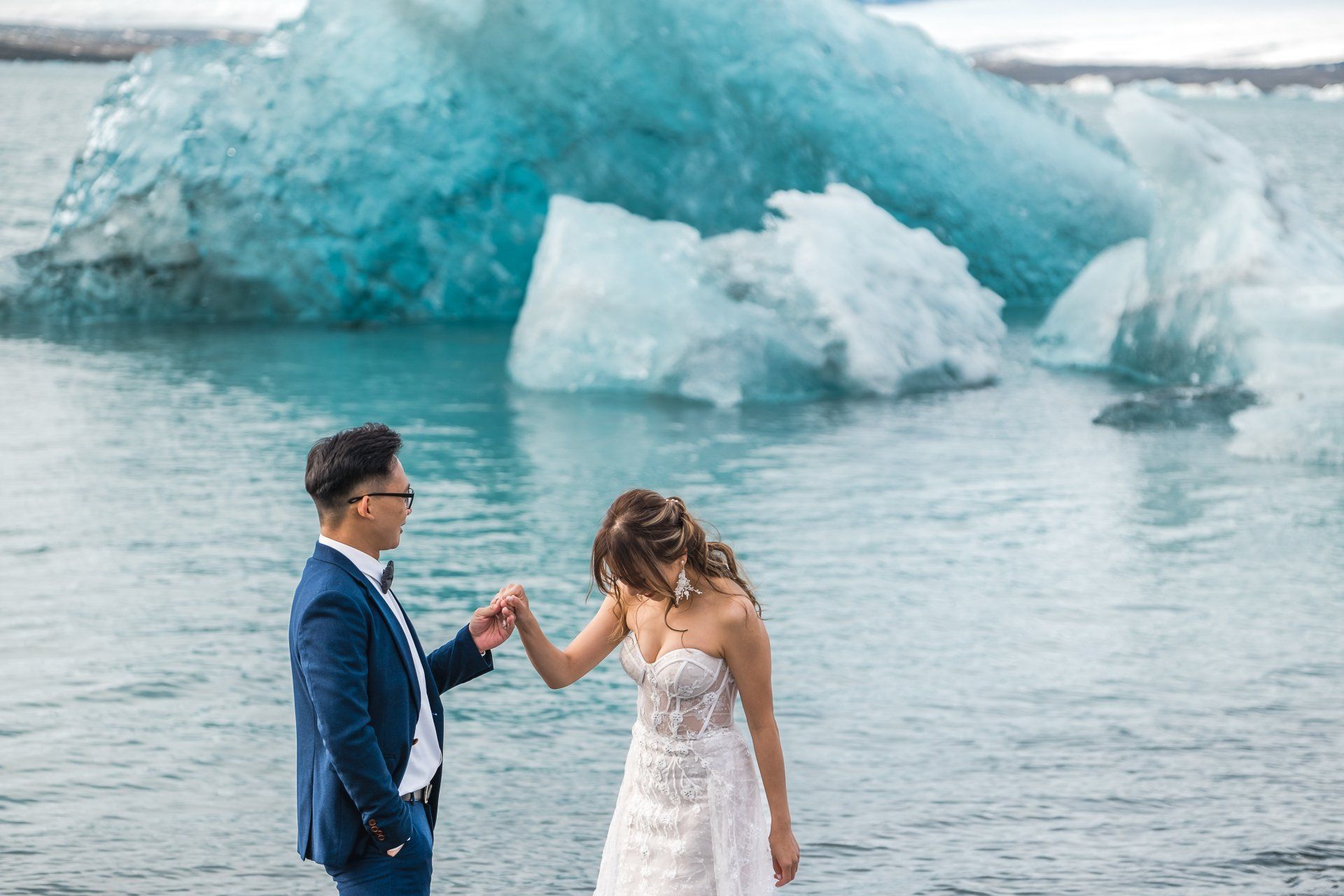 A bride and groom are holding hands in front of an iceberg in the water.