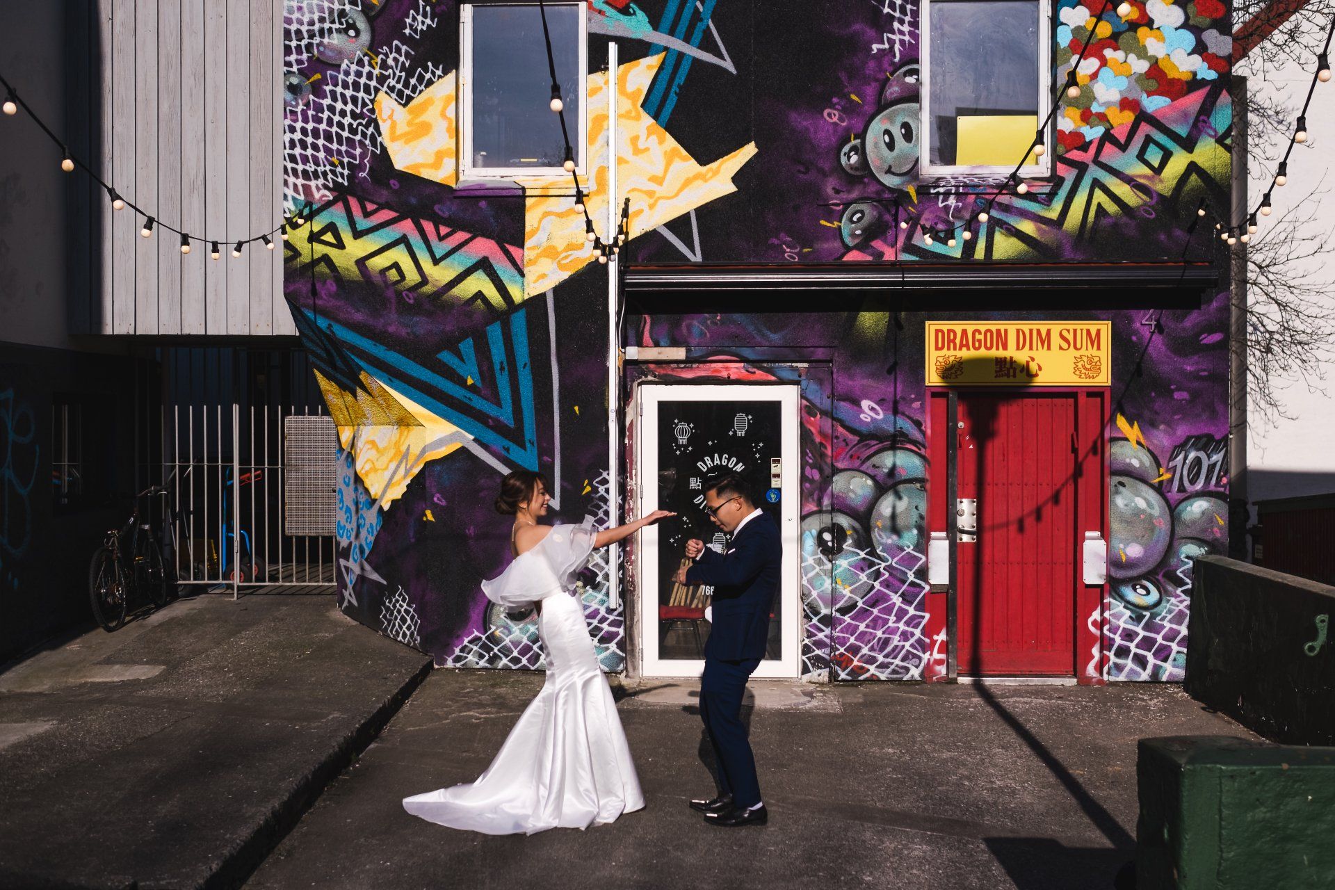 A bride and groom are posing for a picture in front of a building with graffiti on it.