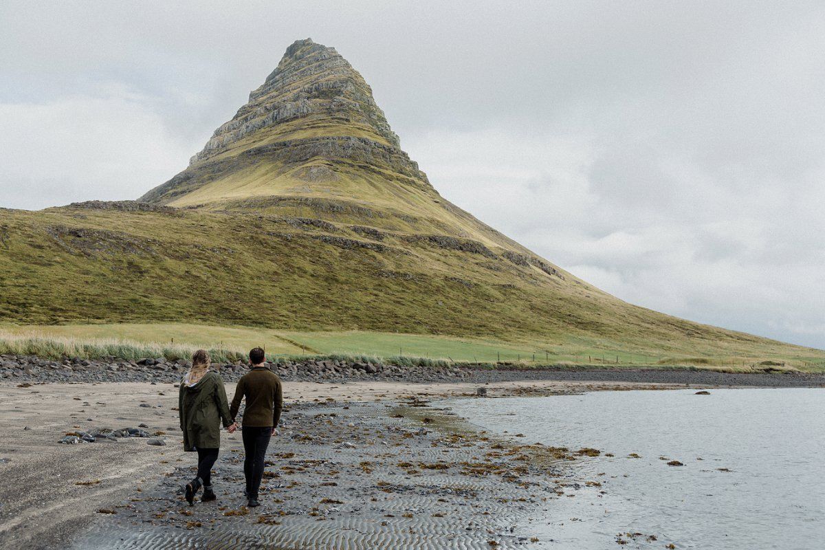 Couple holding hands walking on the beach in front of Kirkjufell in Iceland