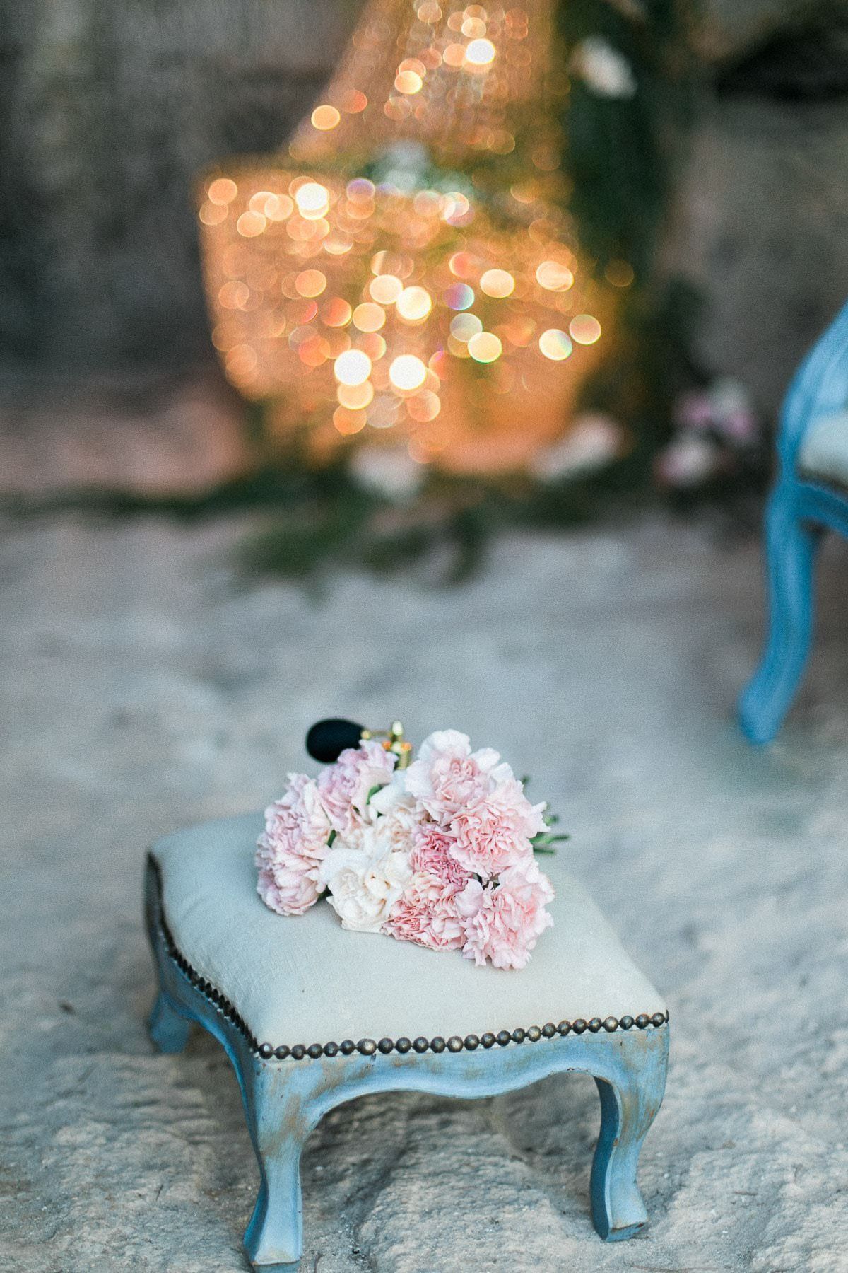 A small ottoman with a bouquet of pink flowers on it.