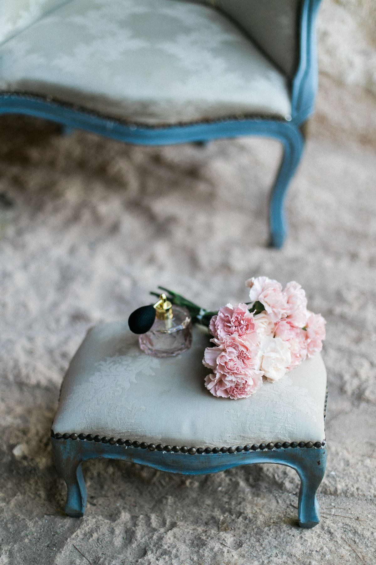 A bottle of perfume is sitting on a small ottoman next to a chair.