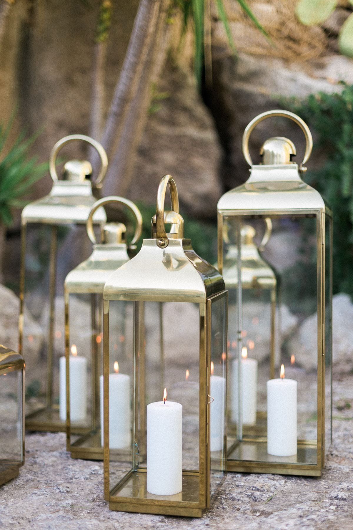 A group of brass lanterns with white candles inside of them.