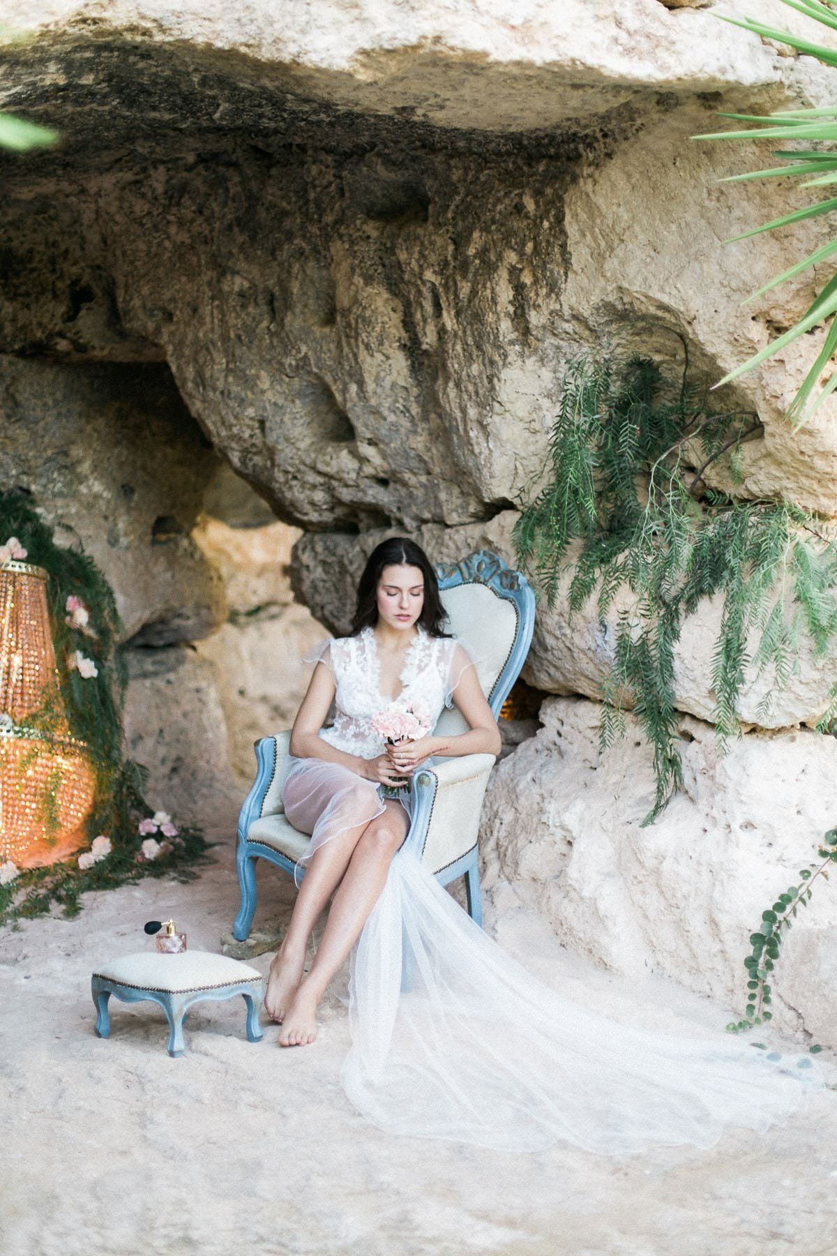 A woman in a white dress is sitting in a chair in a cave.