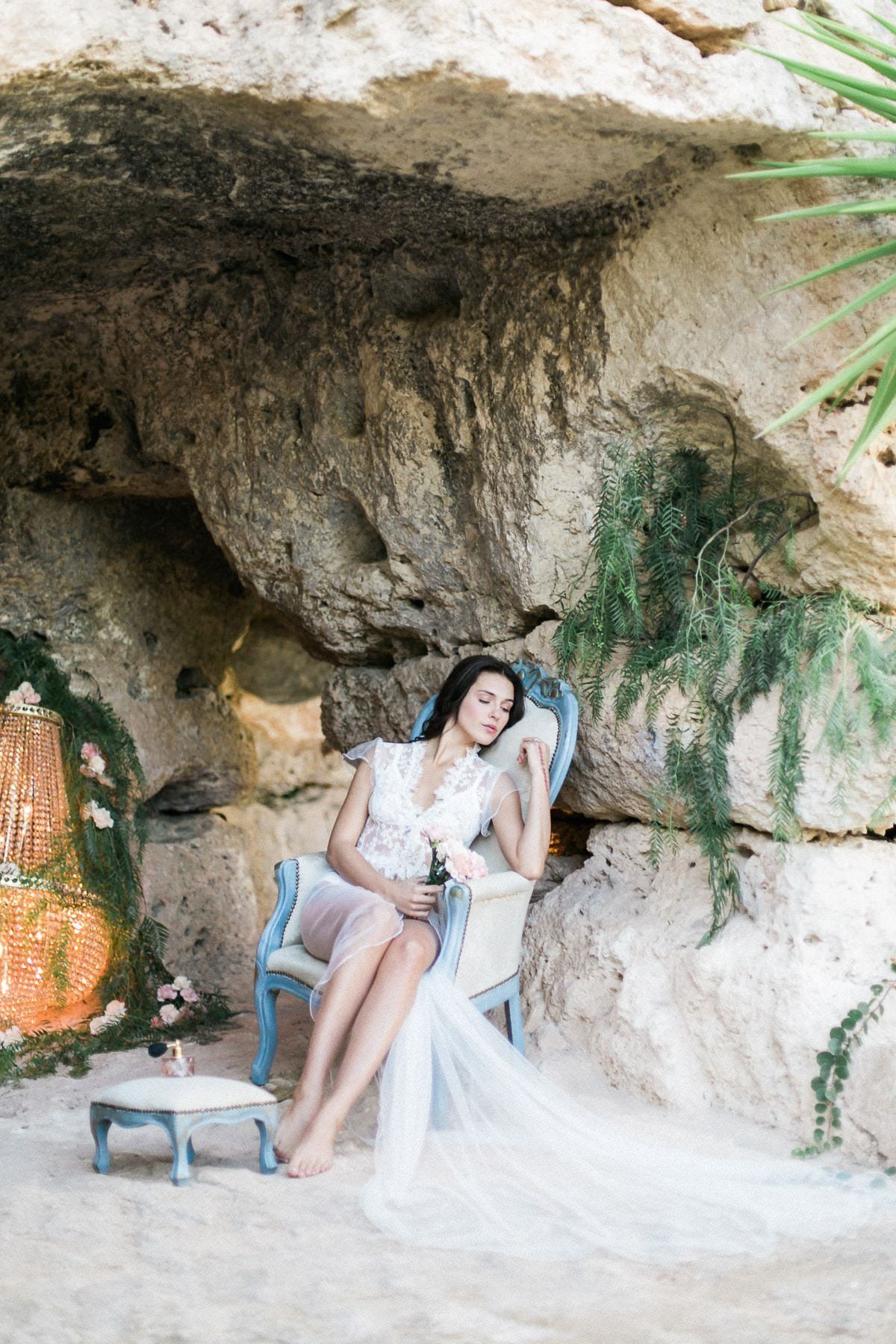 A woman is sitting in a chair in a cave holding a glass of wine.