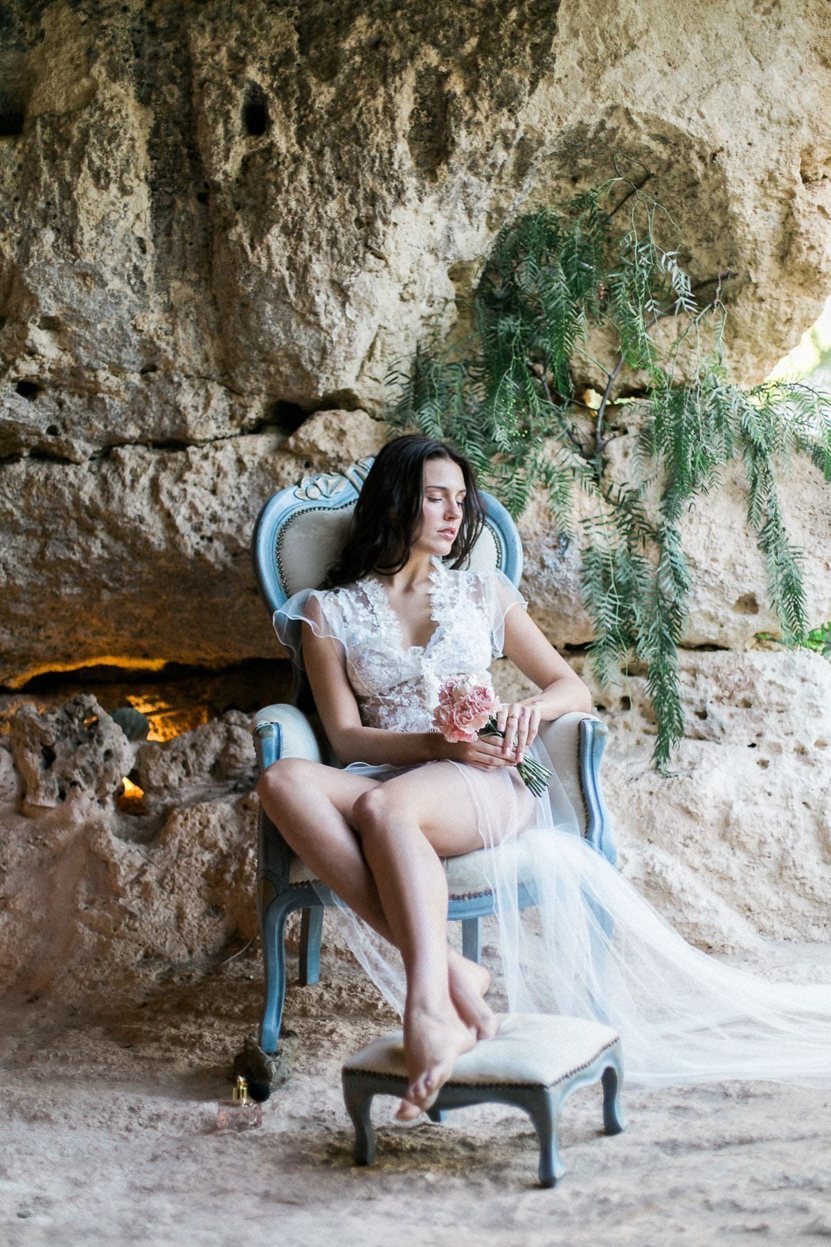 A woman in a white dress is sitting in a chair in a cave.