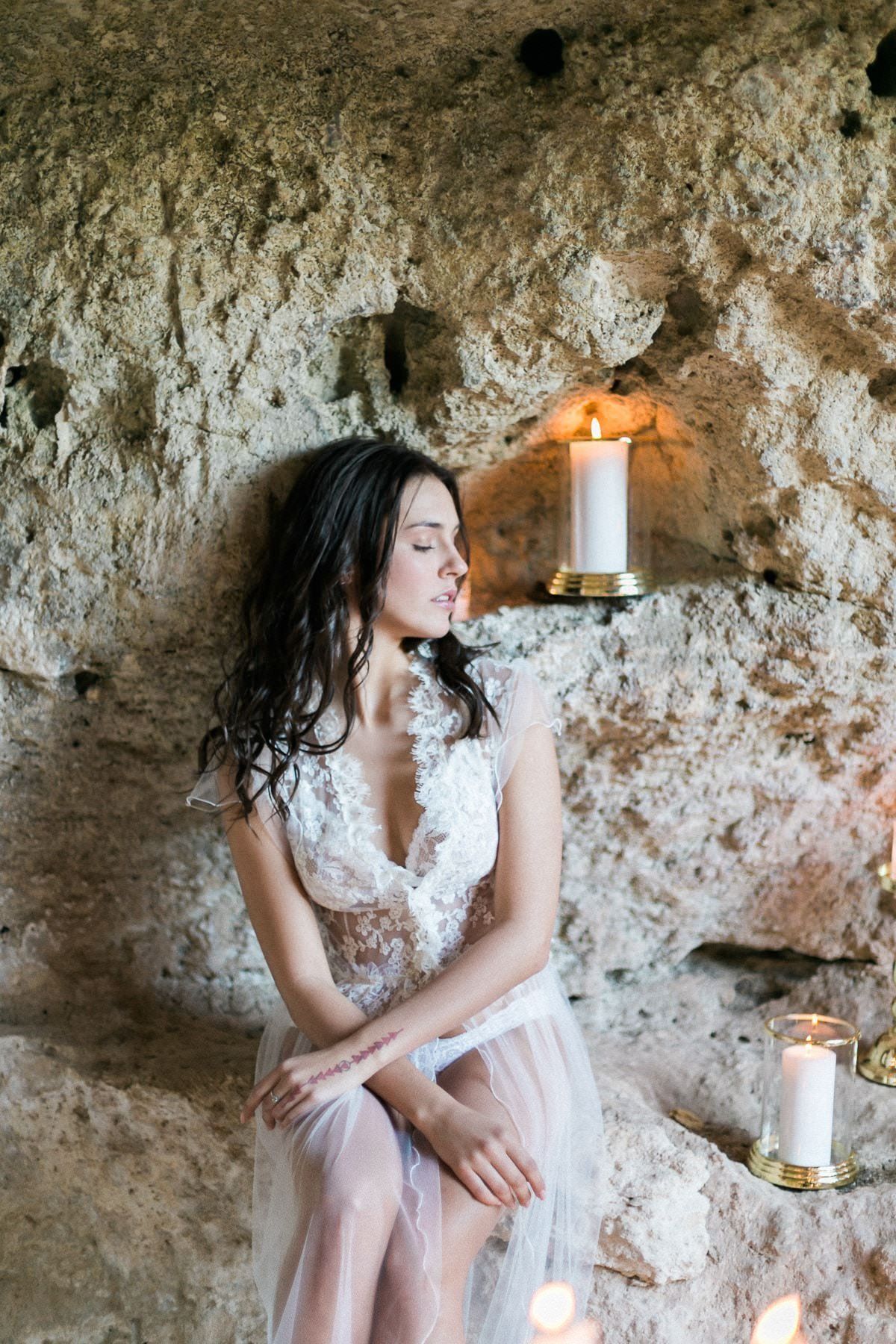 A woman in a white dress is sitting in a cave next to candles.